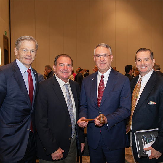 TADA 110th Anniversary Conference and Board Meeting; Four men in suits stand together at a formal event, smiling. One holds a gavel, indicating leadership or a ceremonial role. The atmosphere is professional.