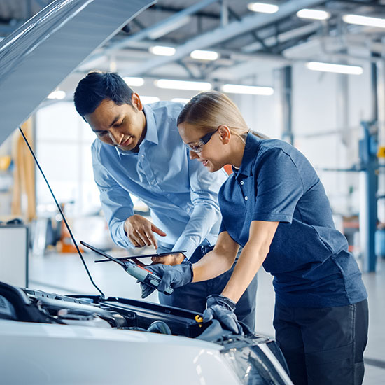 Connecting Employers With Their Future Workforce; A mechanic and a customer stand over an open car hood in a garage, discussing details. The atmosphere is collaborative and professional.