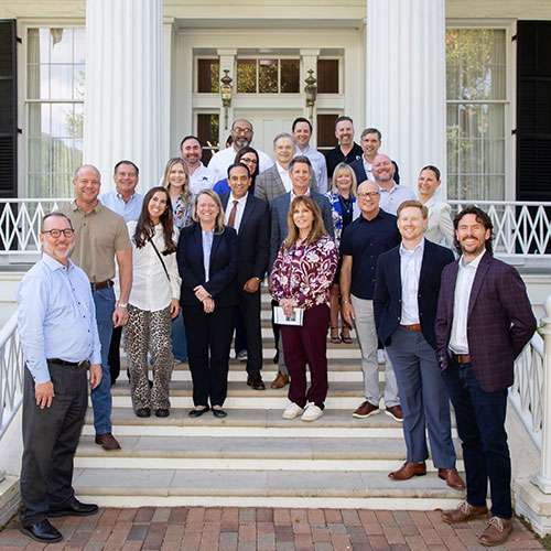 TADA Leadership Network; A diverse group of 23 adults, dressed in business casual attire, stand together on the steps of a white building with large columns, smiling warmly.