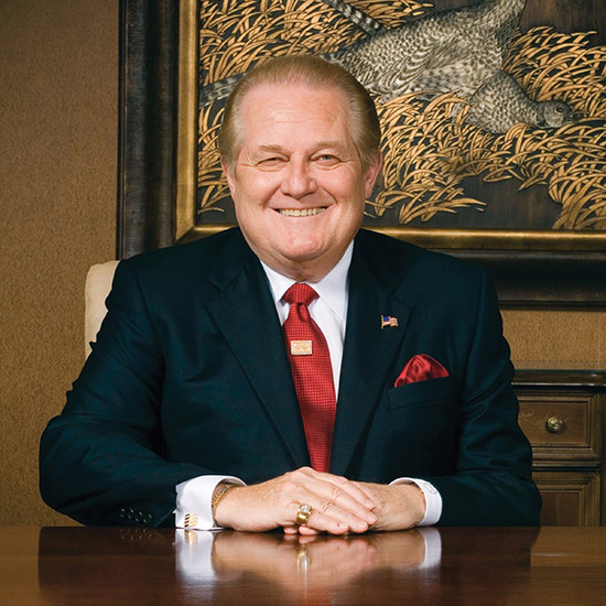TADA Legend Marvin Rush; Smiling man in a suit with red tie and pocket square sits at a desk. Background features a decorative framed artwork depicting birds and foliage.